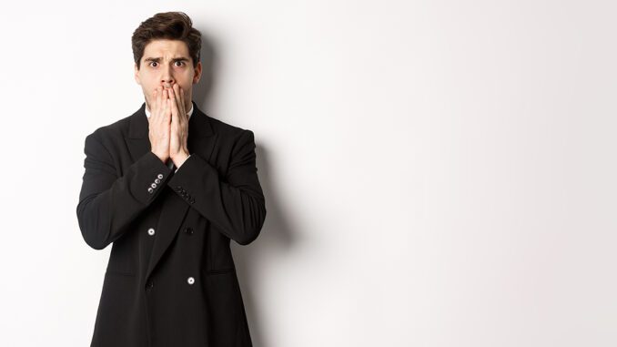Portrait of shocked handsome businessman in suit, reacting to terrible situation, gasping and covering mouth with hands, standing startled against white background
